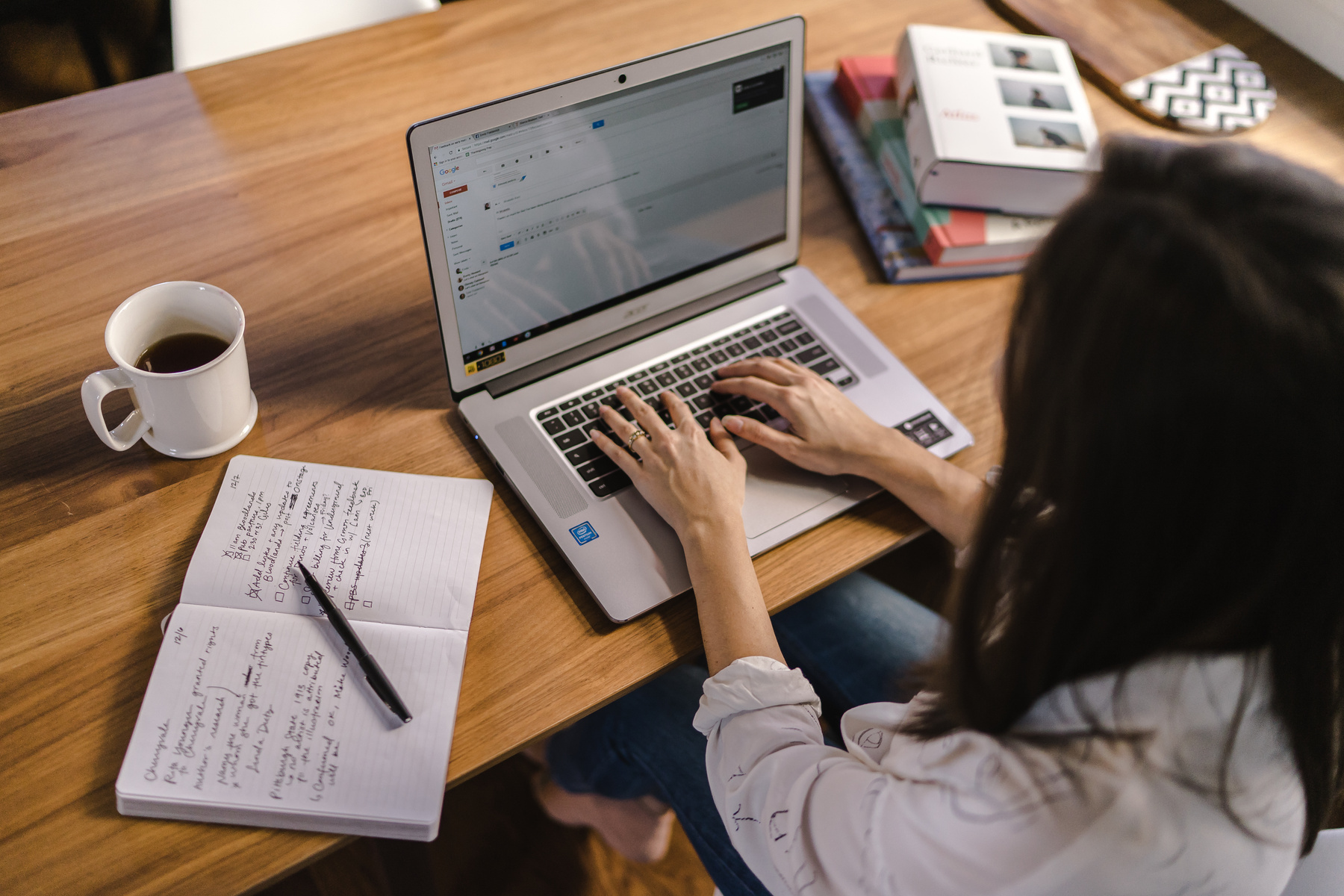 Woman Working on Laptop on Desk with Coffee and Notebook